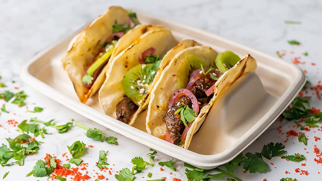 Three bulgogi steak street tacos with pickled onion, kiwi, and sesame seeds on a serving tray