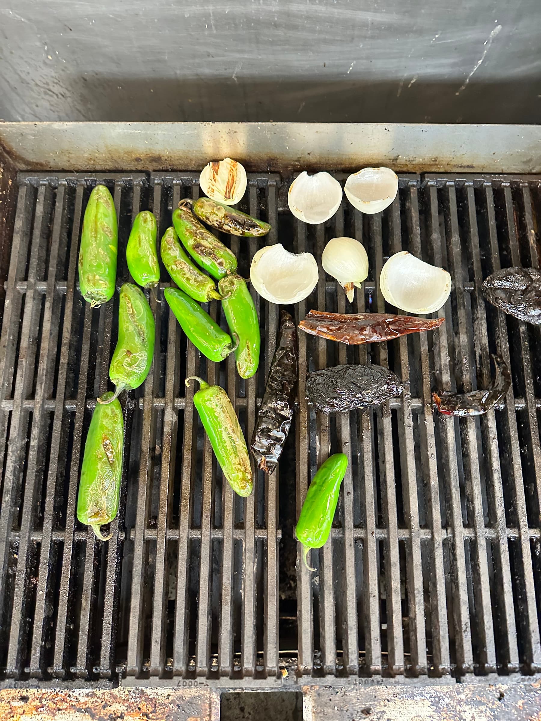 Halved onions, green chiles, and dried chiles charring on the grill grates